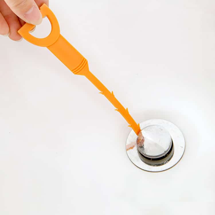 Furet de Nettoyage pour Canalisation orange à barbes tenu à la main au dessus d'une bonde blanche