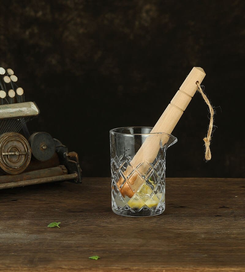 Pilon en bois clair à cordelette en jute posé dans un verre à mélange avec zeste d'orange et glaçon