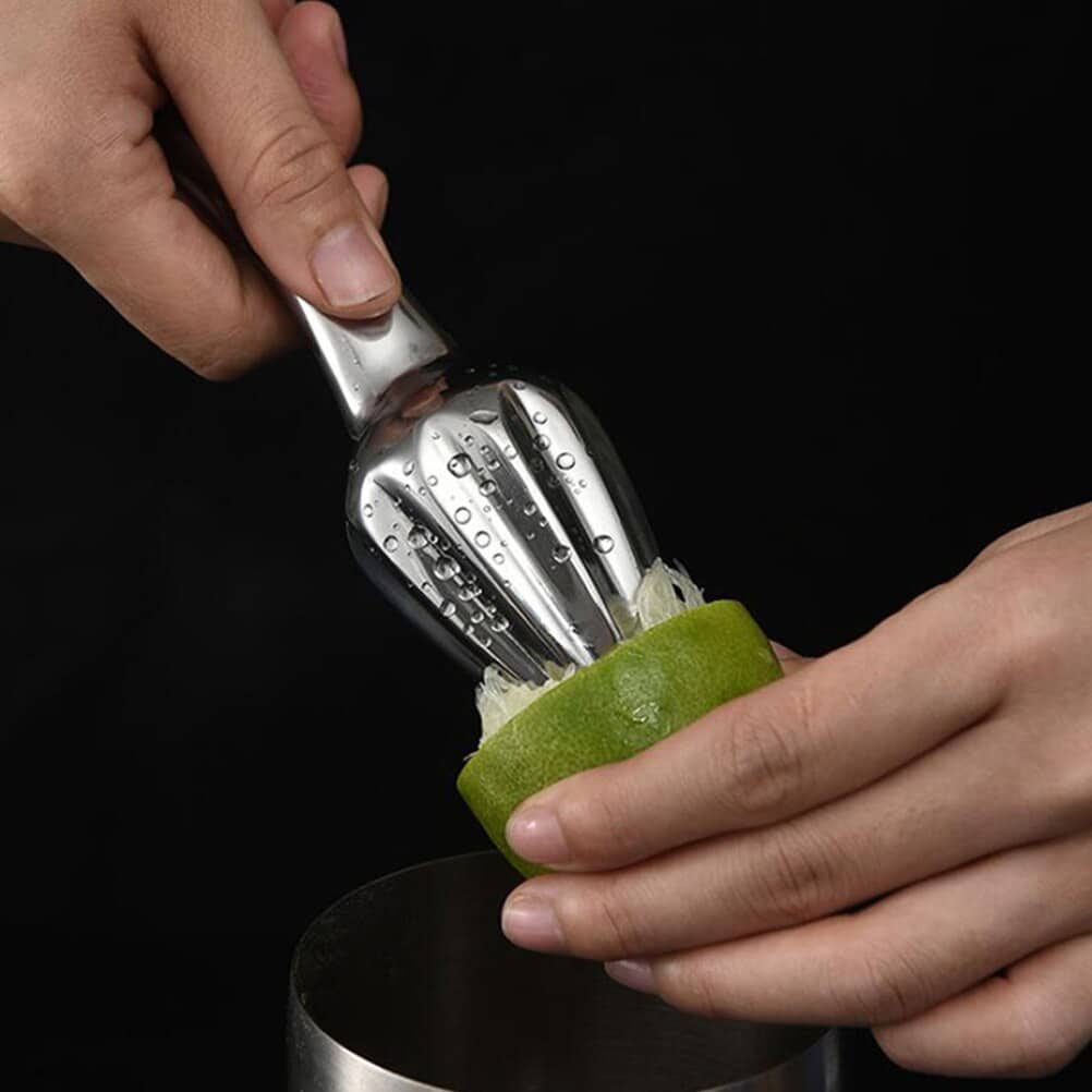 Presse agrume manuel vintage en métal poli enfoncé et tourné dans un demi citron vert au dessus d'un verre