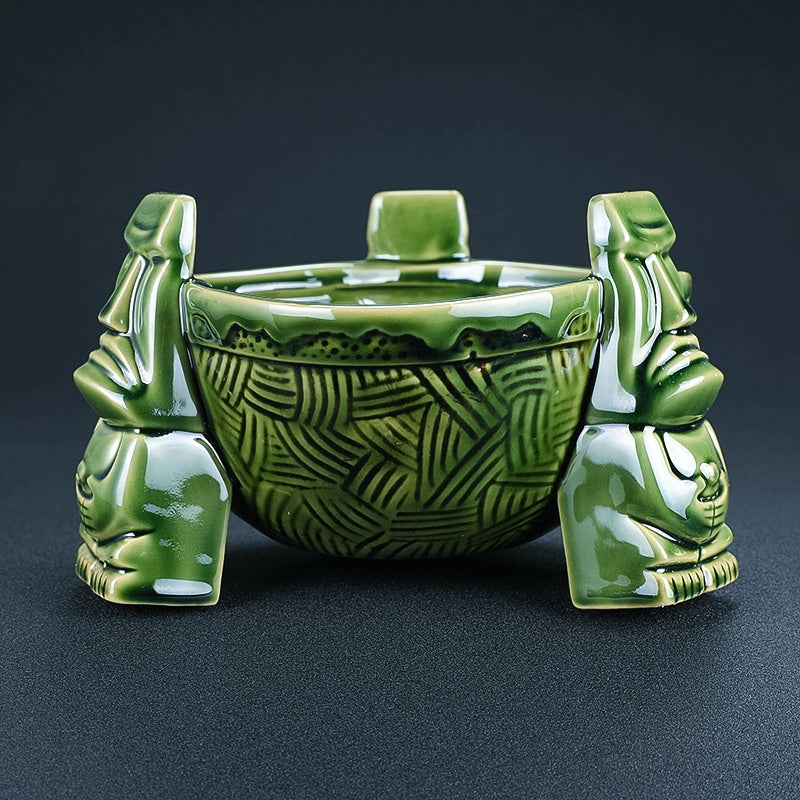 Récipient en céramique tiki vert vide, vasque gravée de motifs tressés et statues moaï sur fond noir