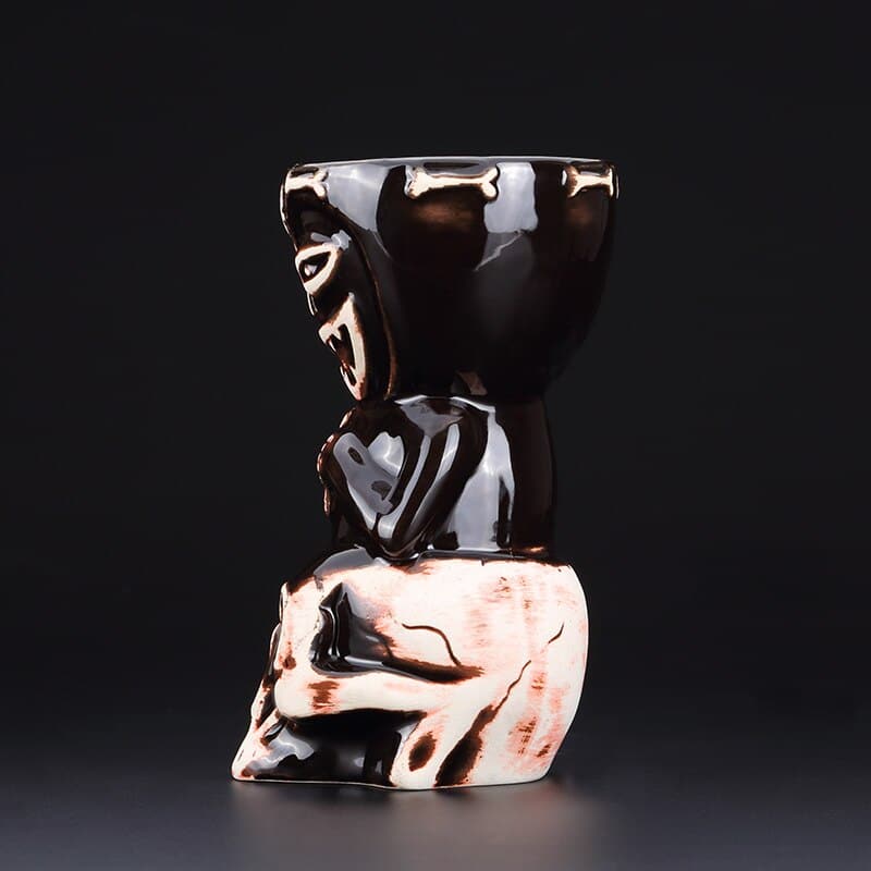 Verre Cocktail Tiki noir laqué vu de côté, dieu tiki assis sur un crâne, reflets cuivrés, fond gris