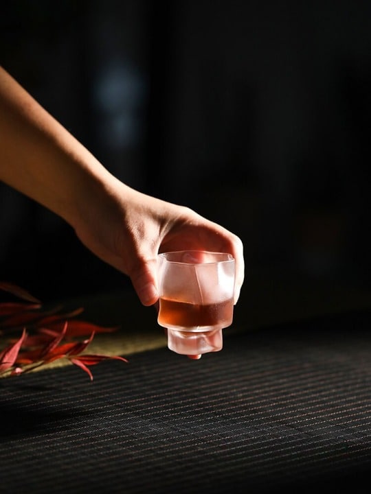 Verre Shooter Design givré tenu en main avec liquide rosé, surface froissée façon impacts, fond sombre