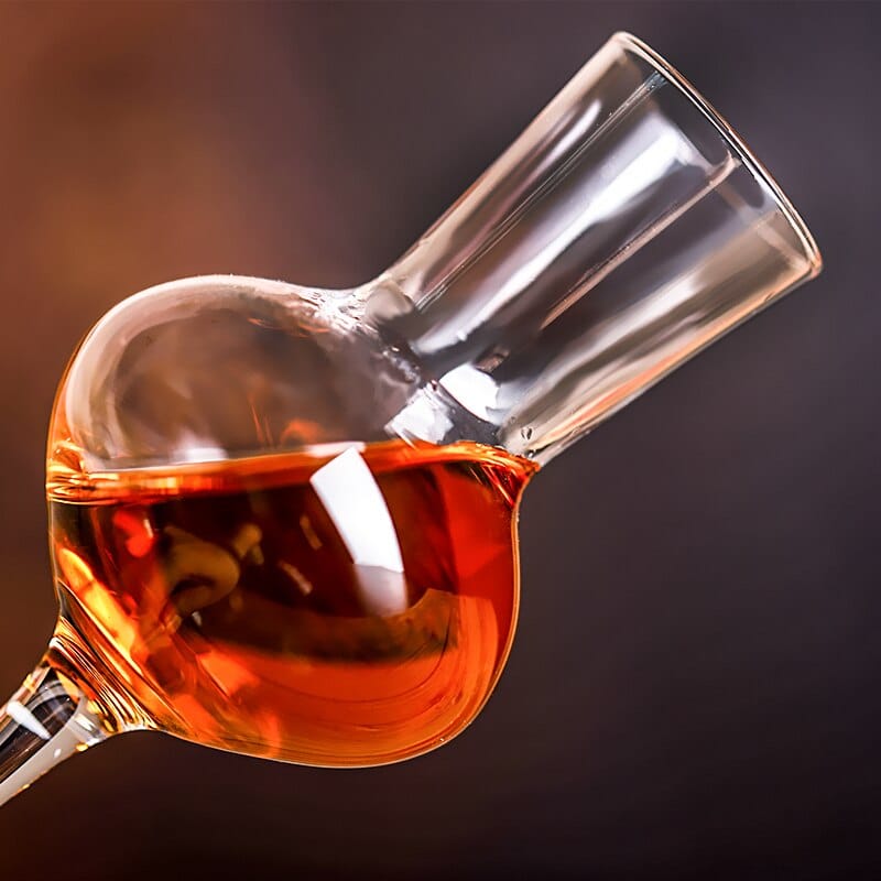 Verre à whisky long incliné, cheminée haute et calice rempli de whisky ambré en gros plan
