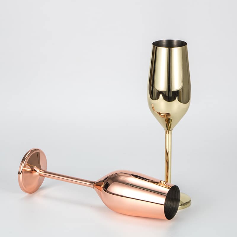 Deux verres à champagne originaux en inox, la flûte dorée debout et la rose gold couchée, sur fond blanc