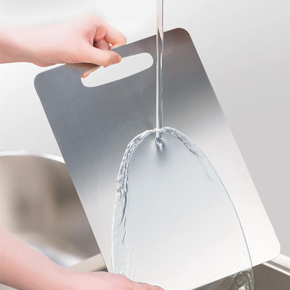 Planche à découper en acier inoxydable brossé rincée à l'eau au dessus d'un évier, tenue par la poignée