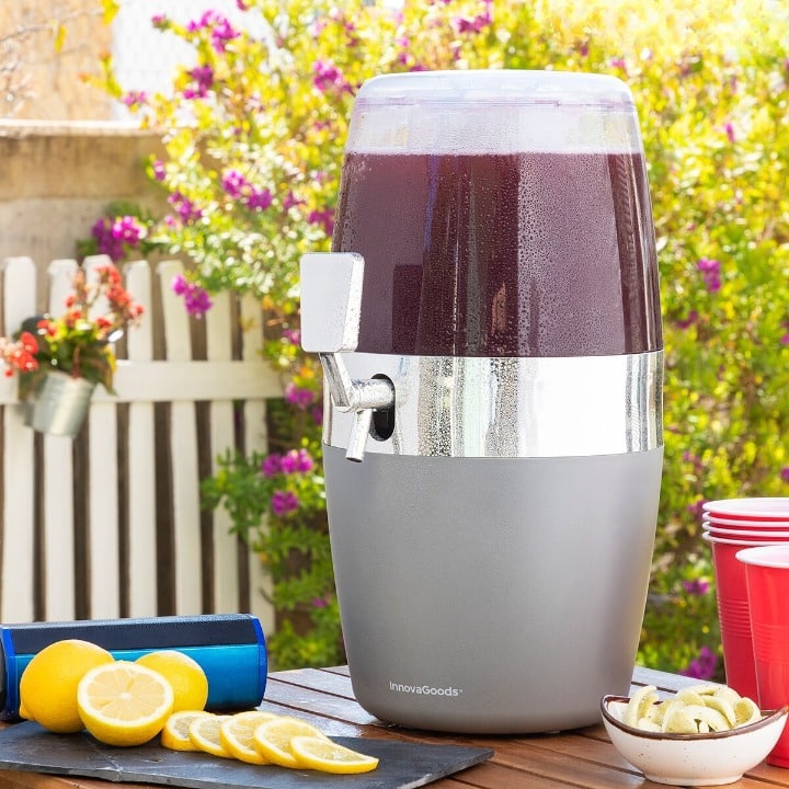 Distributeur de boisson pour particulier rempli d’une sangria, posé sur une table de jardin avec citrons et gobelets