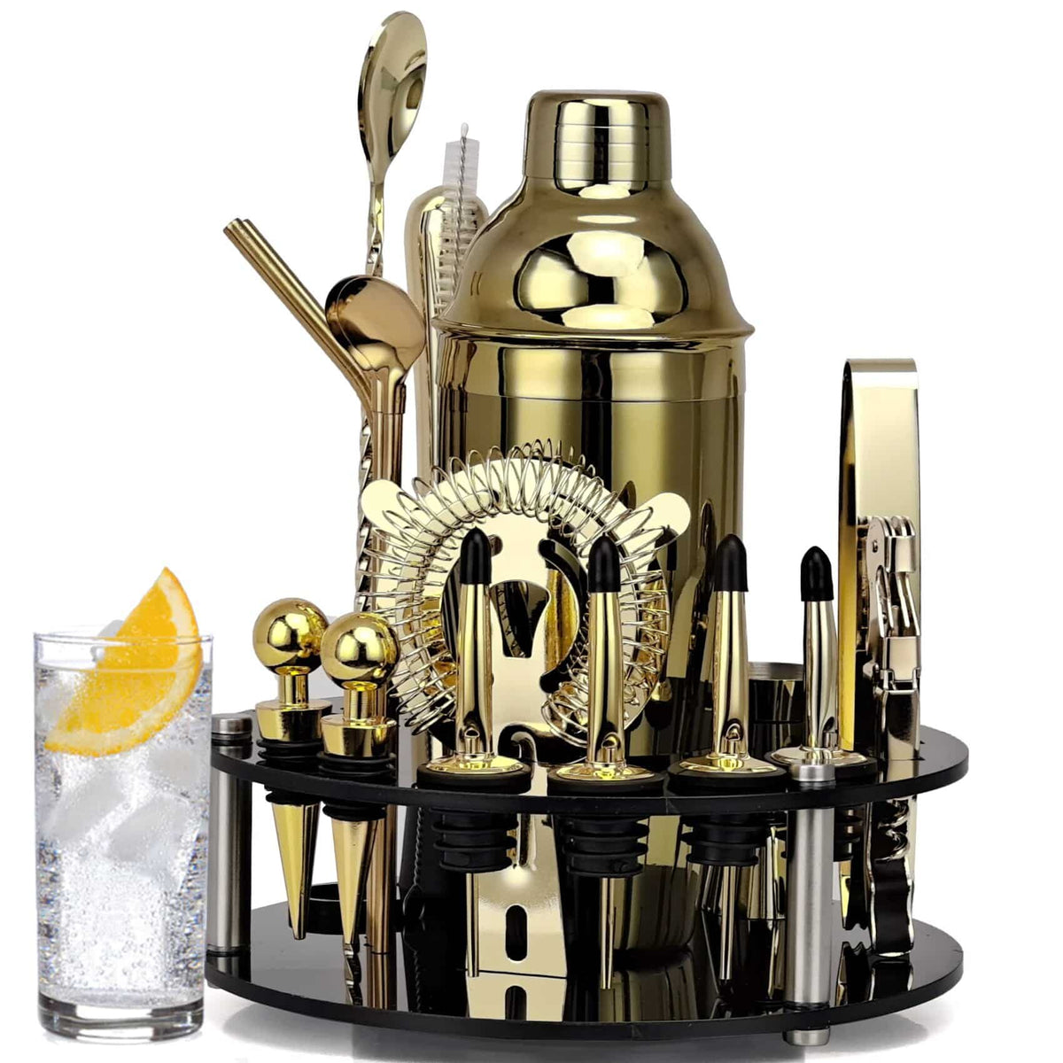 Kit cocktail or avec shaker continental doré sur son support, à côté d’un verre highball garni d’orange