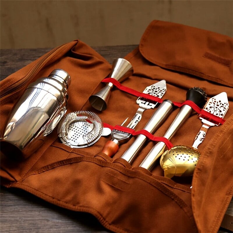 Kit cocktail voyageur ouvert sur une table en bois, shaker, passoire et doseur inox maintenus par des élastiques rouges
