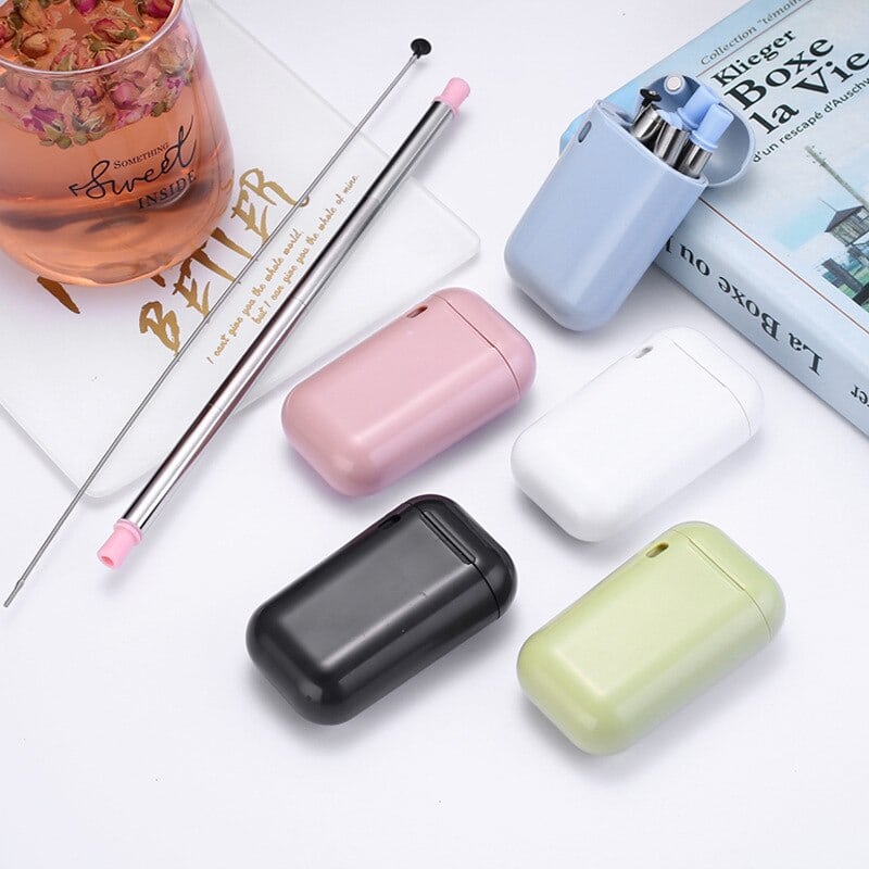 Pailles en inox pliables et leurs étuis bleu, rose, blanc, noir et jaune près d'un verre de thé aux fleurs