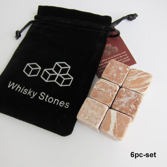 Six pierres à whisky scandinaves en pierre veinée saumon posées près du pochon velours Whisky Stones