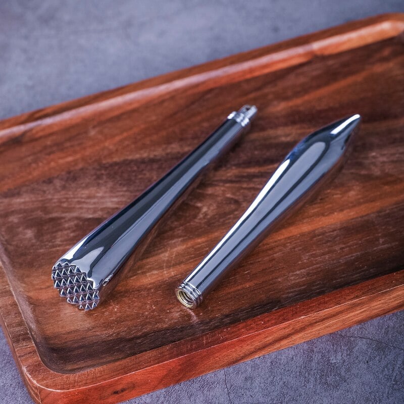 Pilon cocktail design chromé dévissé en deux parties, tête à picots et pointe, sur une planche en bois foncé
