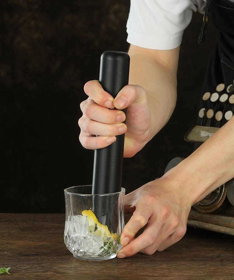Pilon pour cocktail noir mat écrasant zeste de citron et menthe dans un verre à facettes glacé
