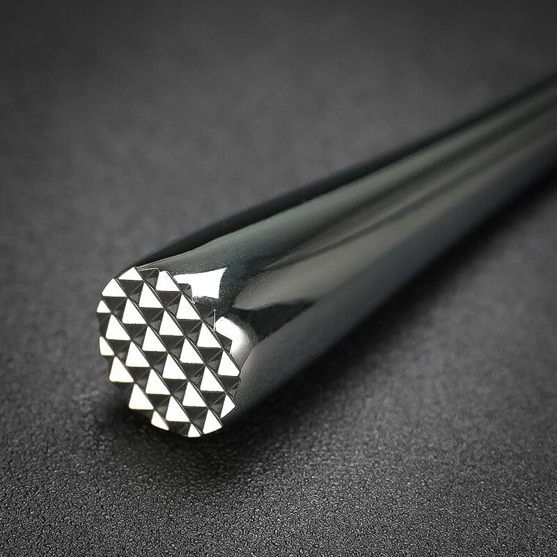 Gros plan sur la tête à picots pyramidaux du pilon cocktail design en acier chromé brillant sur fond noir