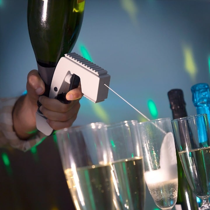Main tenant le pistolet à alcool avec sa bouteille retournée, servant une rangée de flûtes de champagne