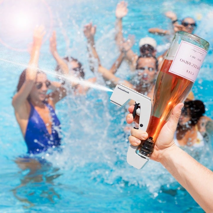 Pistolet à alcool projetant un jet de vin rosé au dessus d’une piscine pendant une pool party