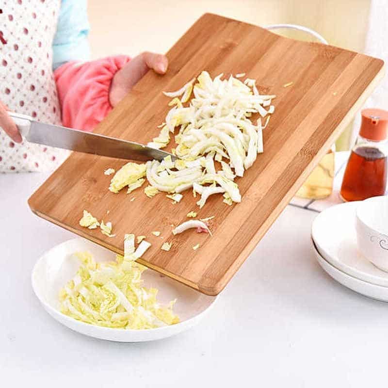 Découpe de chou émincé sur une planche à découper en bois de bambou versé dans un plat blanc en cuisine