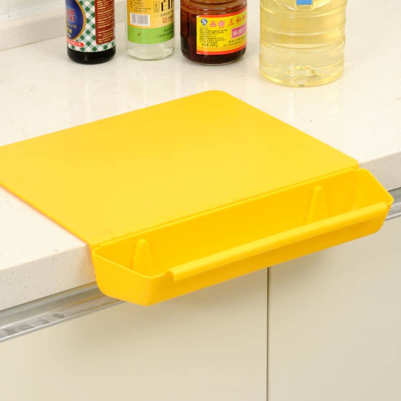 Planche à découper en silicone jaune avec bac de récupération accrochée au rebord du comptoir de cuisine