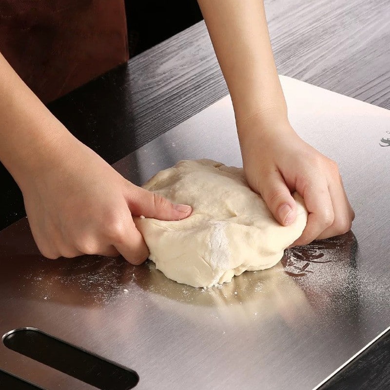 Planche à découper en acier inoxydable utilisée pour pétrir une boule de pâte farinée sur un plan de travail