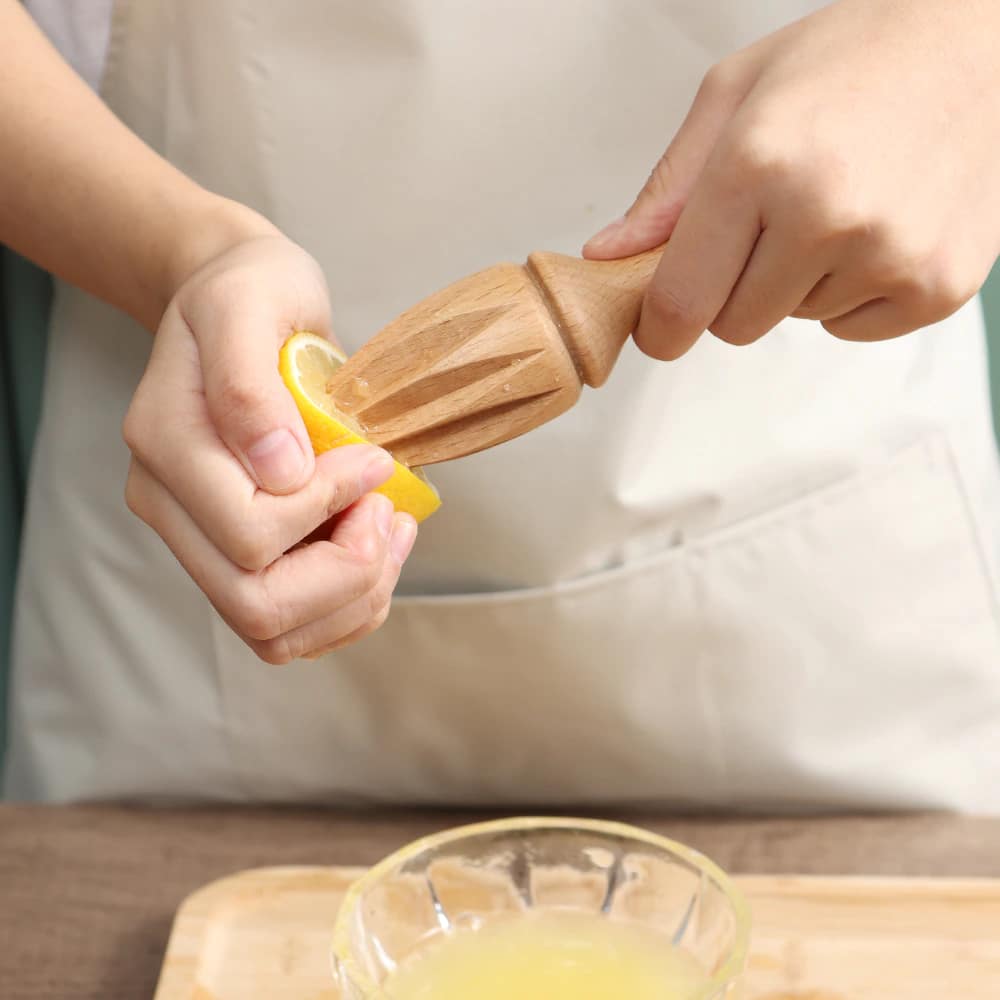 Mains pressant un demi citron avec le presse agrume manuel bois cannelé au dessus d'un bol de jus