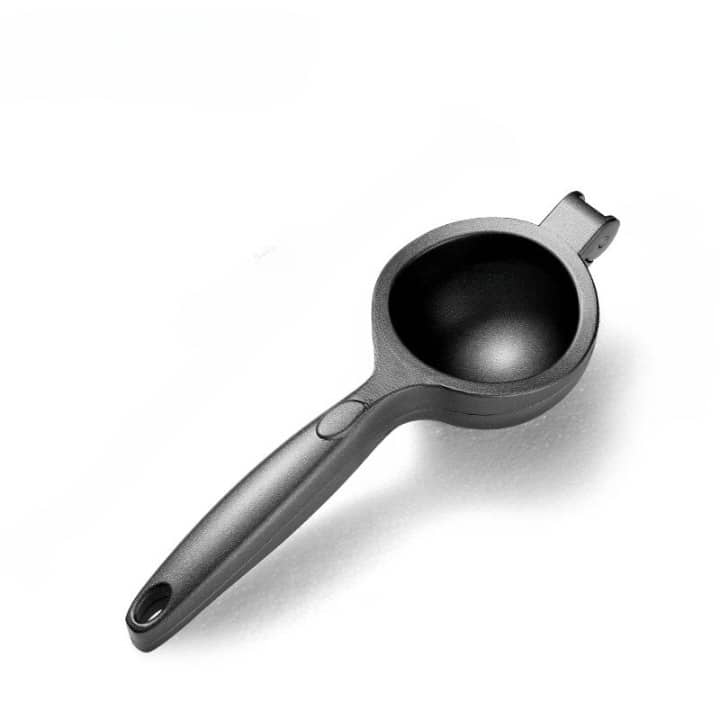 Presse citron design noir pressant un fruit rouge dont le jus coule dans un mug en verre sur fond noir