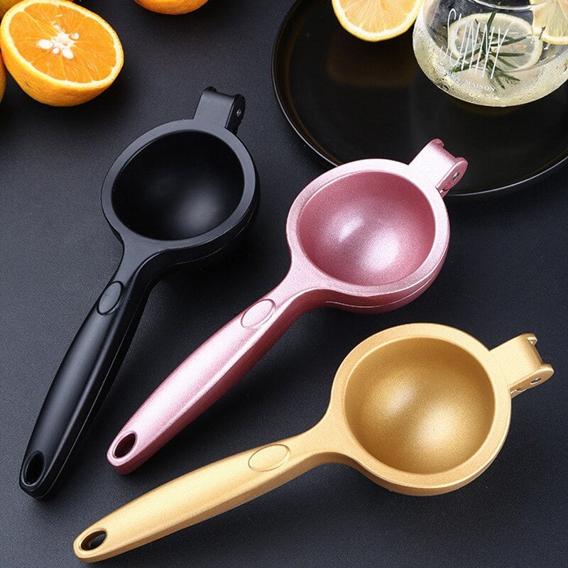 Presse citron design à bras en noir, rose et or posés près d'oranges coupées et d'un verre de boisson