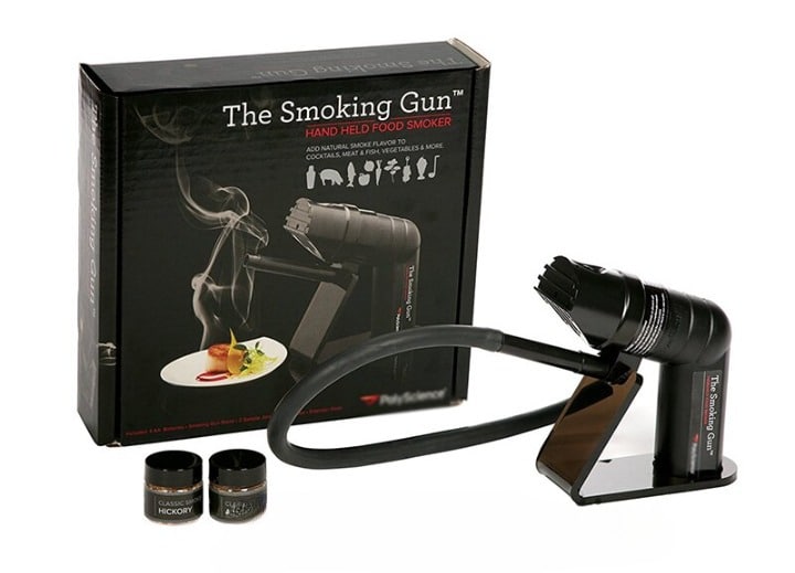 Smoked gun noir avec socle, tuyau et deux pots de copeaux devant sa boîte The Smoking Gun food smoker