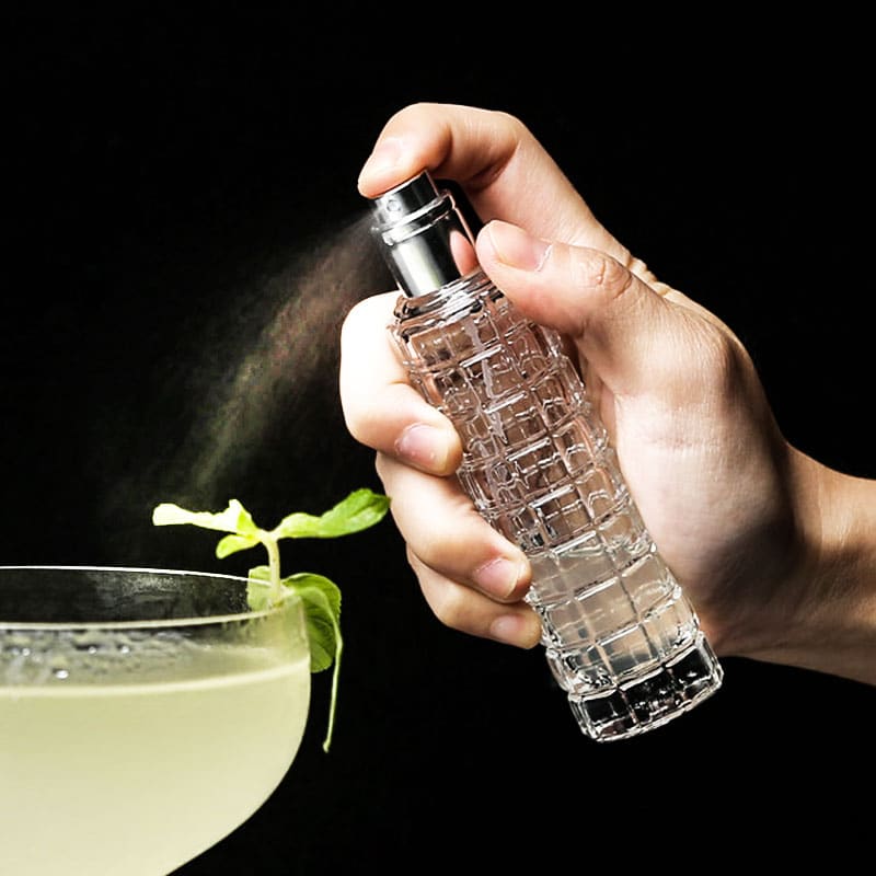 Spray pulvérisateur culinaire en verre texturé vaporisant une brume sur un cocktail pâle à la menthe