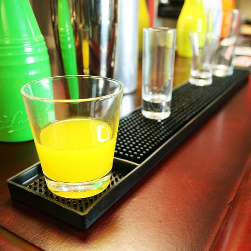 Verre de boisson jaune et shots posés sur un tapis de bar en caoutchouc 8x58 noir le long d'un comptoir