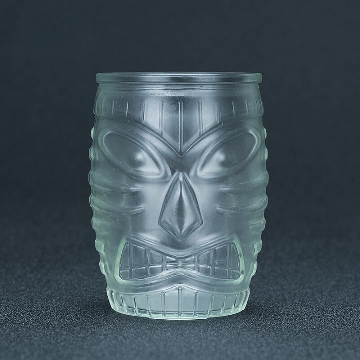 Tiki Verre en verre transparent dépoli au visage tiki moulé, présenté vide sur fond gris foncé