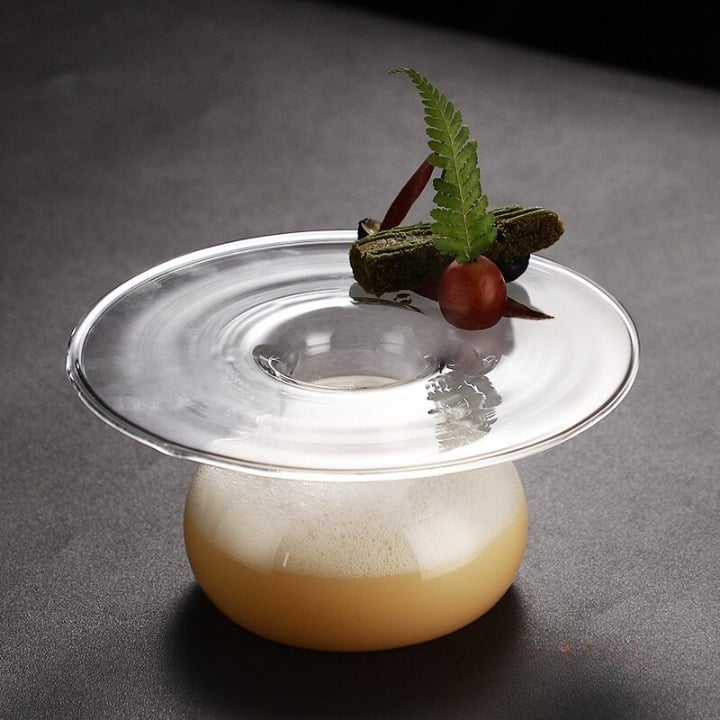 Verre à Cocktail Géant XXL soucoupe en verre, cocktail ambré mousseux garni de fougère et d'une baie, fond gris