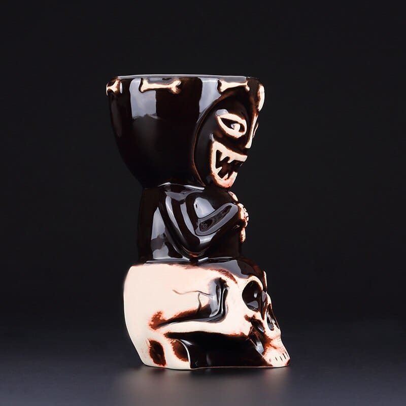 Verre Cocktail Tiki en céramique noire de profil, base en forme de crâne blanc et cuivré, fond gris