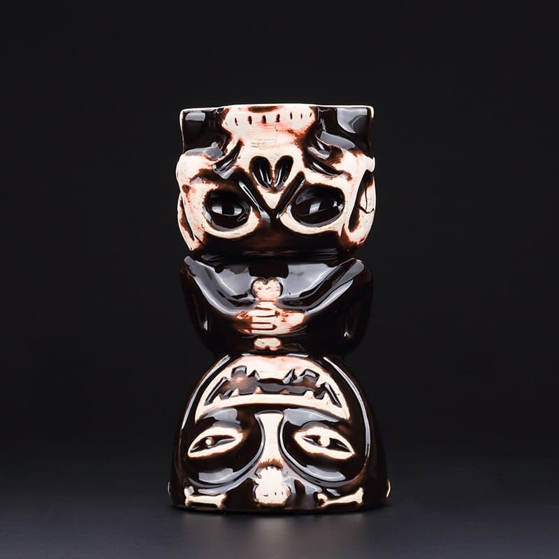 Verre Cocktail Tiki noir vu de face, visage de dieu tiki grimaçant au dessus d'un crâne, fond noir