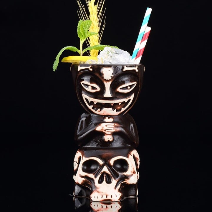 Verre Cocktail Tiki en céramique noire sur base crâne, glace pilée, menthe et pailles colorées, fond noir