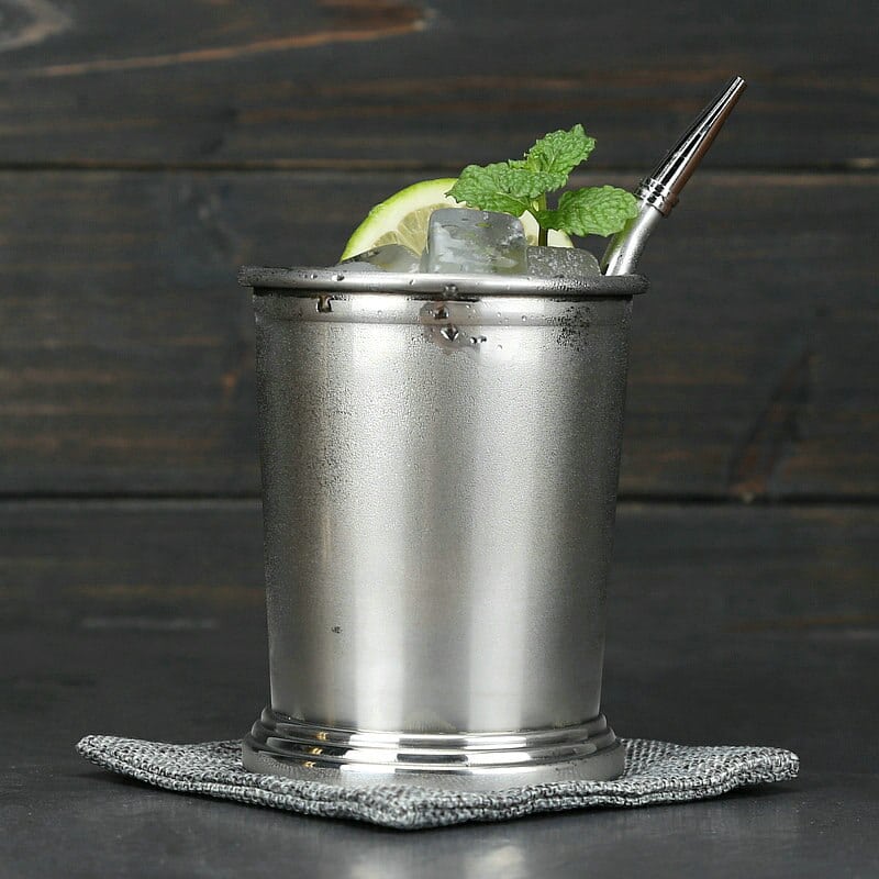 Verre Moscow Mule Julep argenté à base annelée, glace, citron vert, menthe et paille métallique sur fond bois