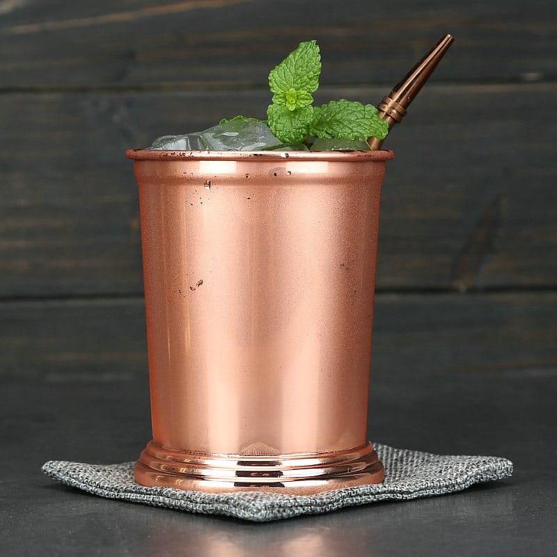 Verre Moscow Mule Julep cuivré rose gold garni de glace et menthe, paille assortie sur un dessous gris