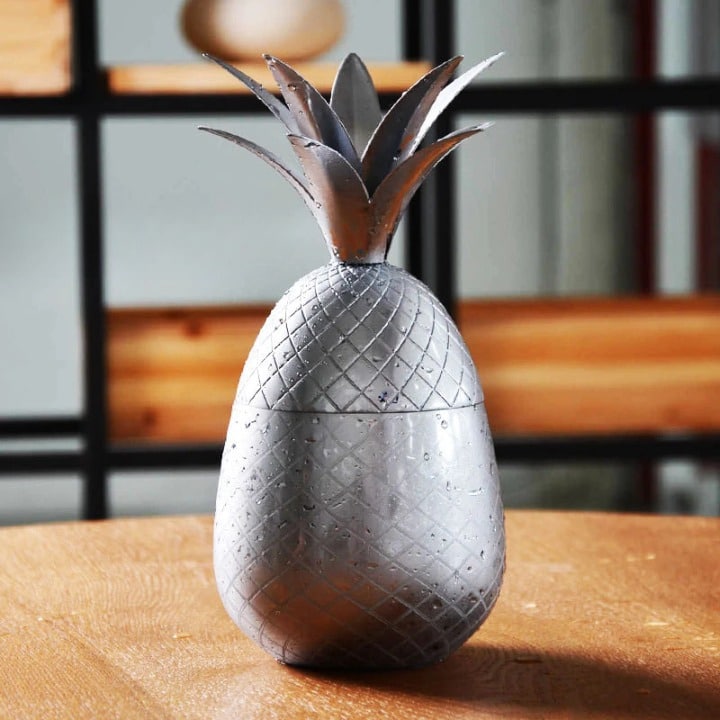 Verre Moscow Mule Ananas gris argenté fermé par sa coiffe de feuilles, motif quadrillé, sur table en bois