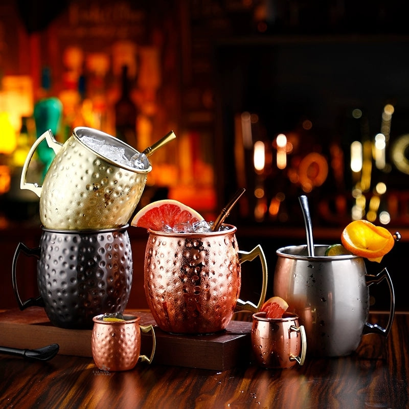 Collection de verres Moscow Mule martelés or, noir, cuivre et argent de plusieurs tailles sur un comptoir de bar