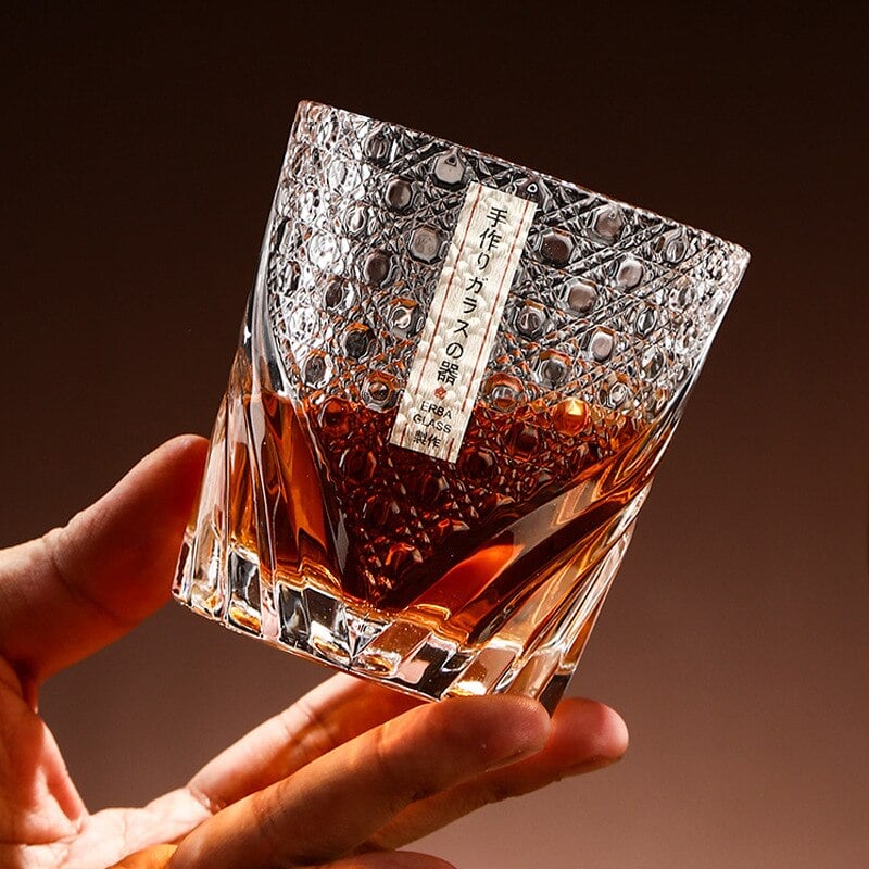 Main tenant un verre whisky luxe en cristal taillé rempli de whisky ambré, motifs à facettes et étiquette japonaise