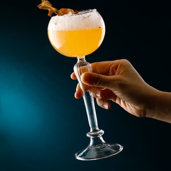 Verre à Cocktail Vintage à pied haut et calice ballon, cocktail orange mousseux tenu en main sur fond bleu