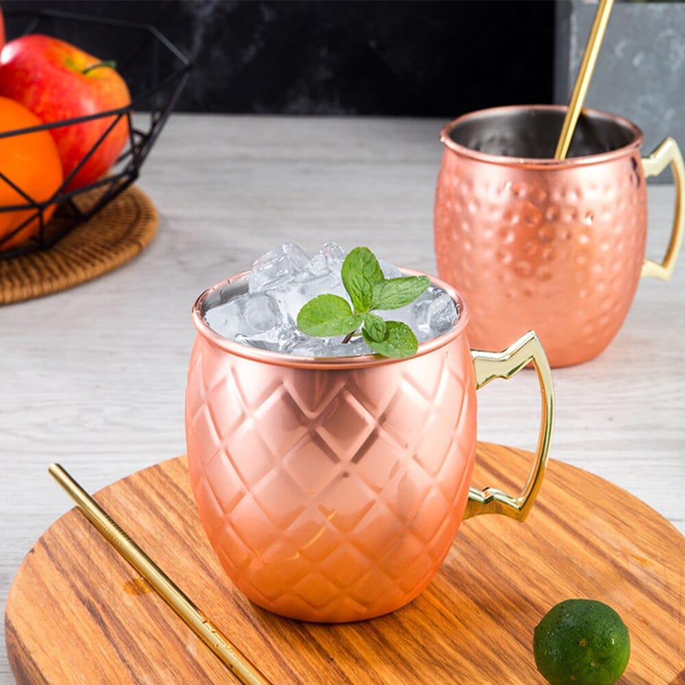 Verre Moscow Mule Design cuivré à losanges gravés rempli de glace et menthe, anse dorée, mug martelé derrière
