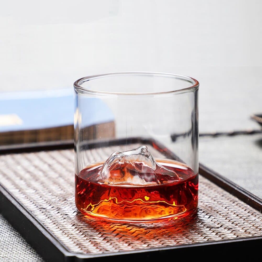 Verre à whisky montagne contenant un cocktail rouge, sommet en relief émergeant du liquide, sur un set de table tressé