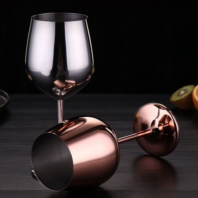 Deux verres à vin originaux en inox, l’argenté debout et le rose gold couché, sur une table noire