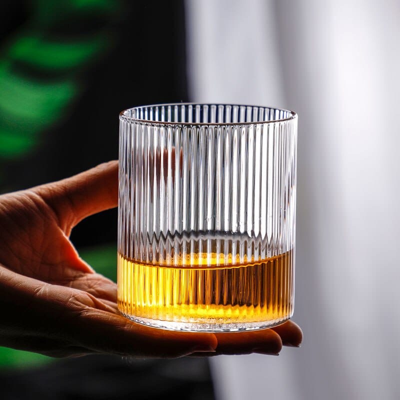 Verre à whisky design aux stries verticales tenu dans une main, fond de whisky doré dans le verre
