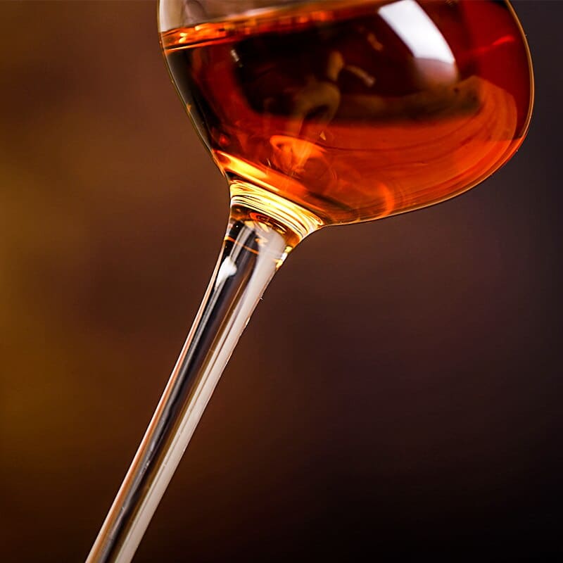 Gros plan sur le pied élancé du verre à whisky long incliné, whisky ambré dans le calice